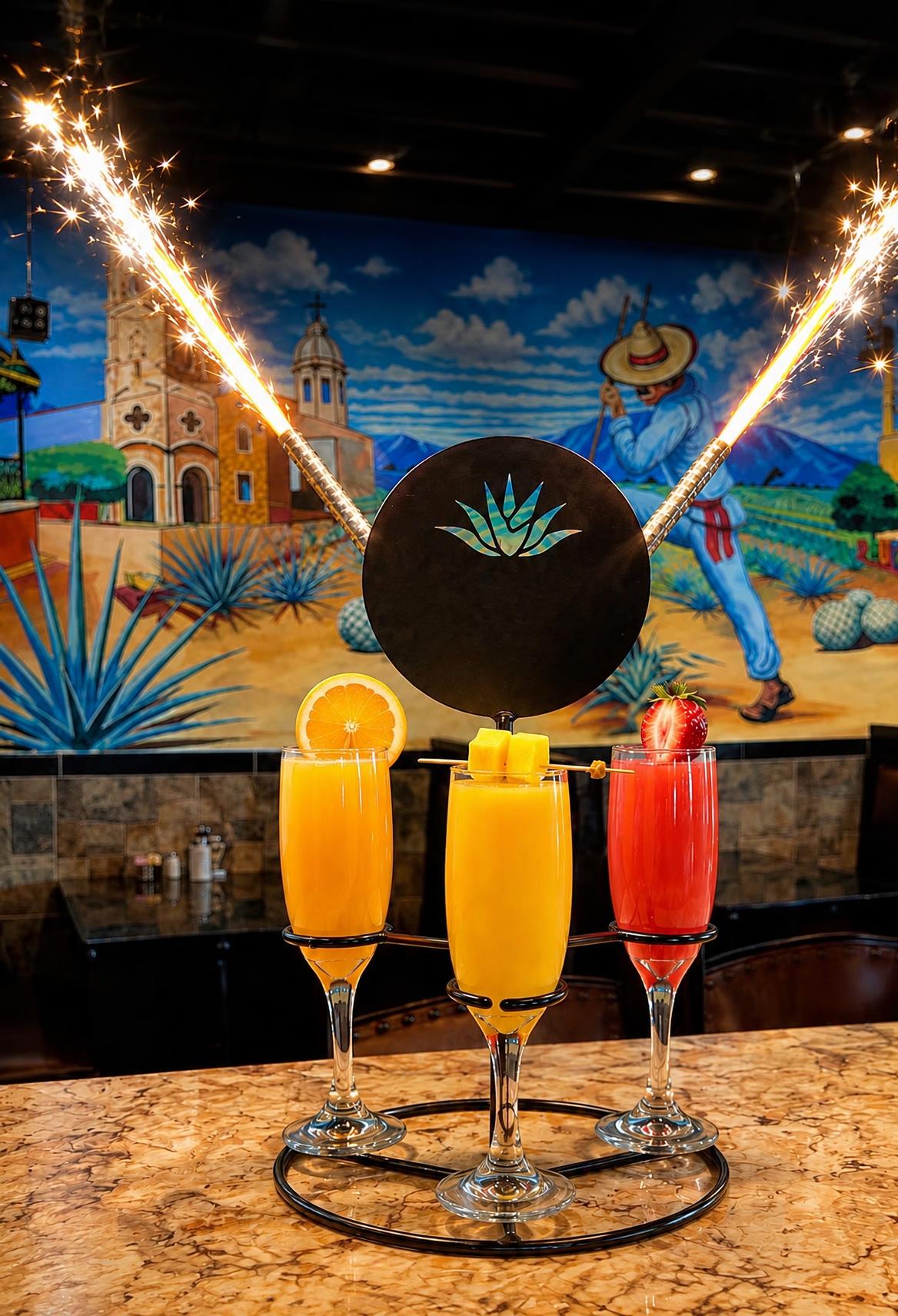 Mimosa flight with orange, mango and strawberry mimosas and lit sparklers in front of the Los Agaves mural